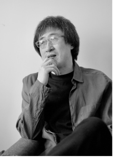 Man with short hair and glasses wearing a dark t-shirt.