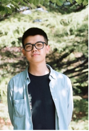Man with short hair and thick frame eyeglasses wearing a blue long sleeve shirt over a black shirt.