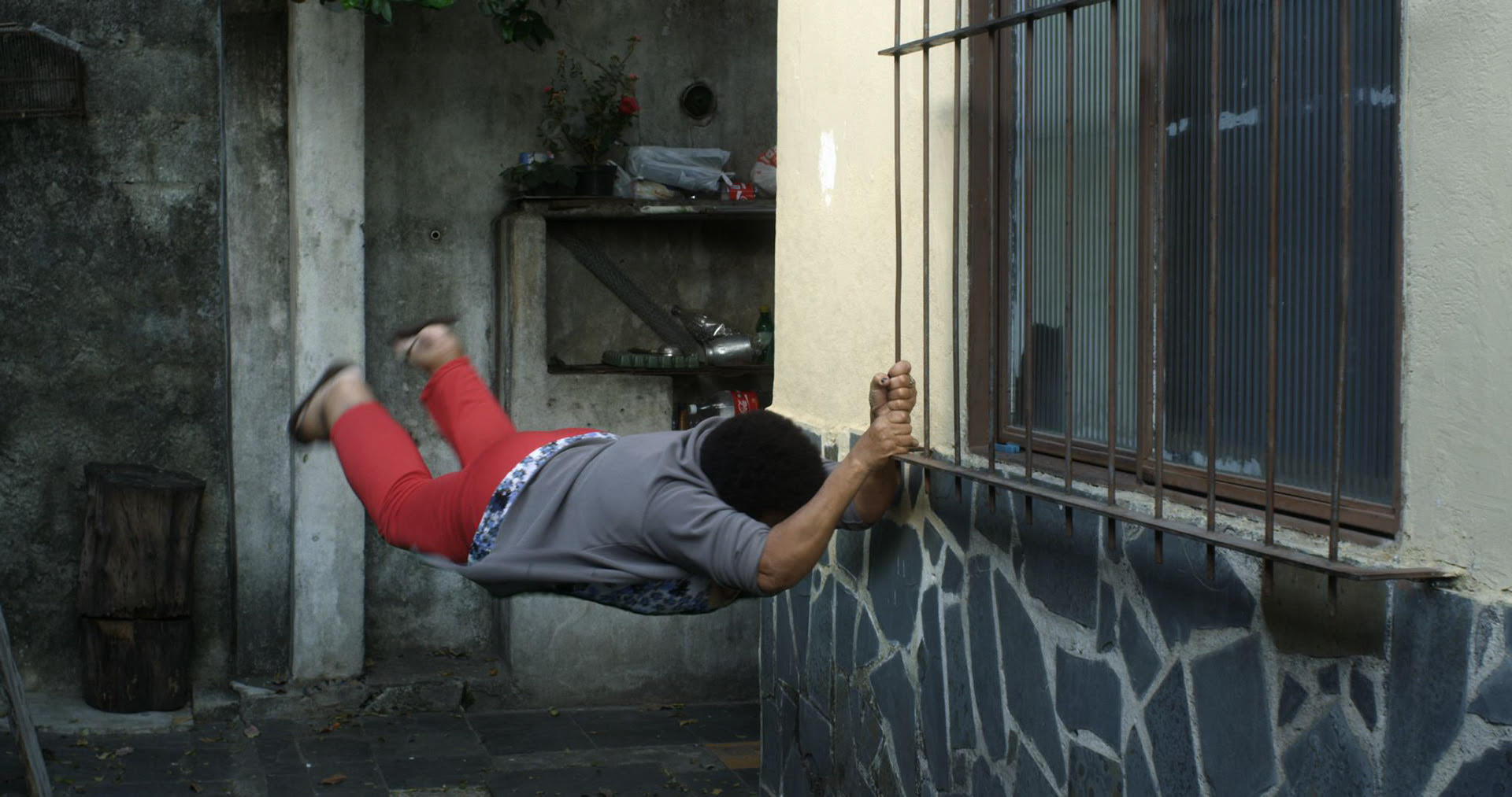 A person hanging from a window grate in mid-motion.