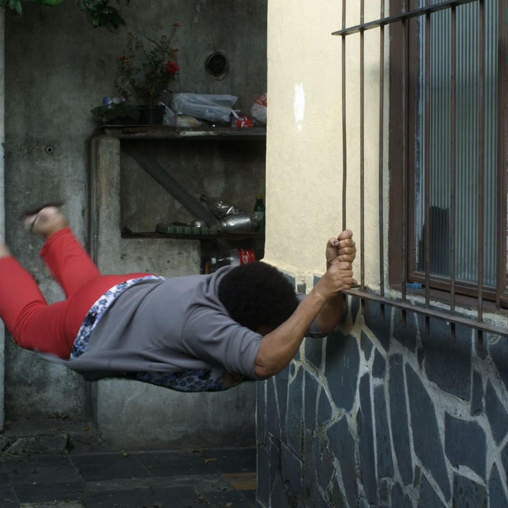 A person hanging from a window grate in mid-motion.
