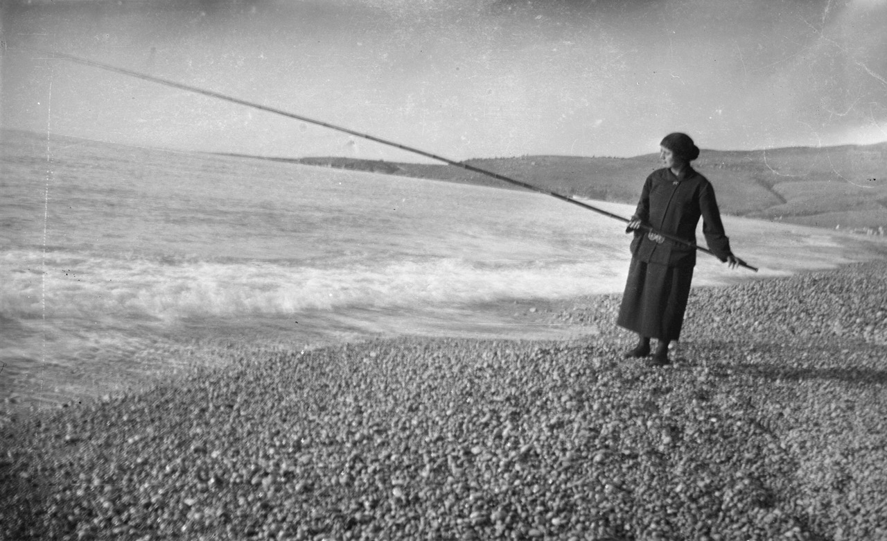 Woman on a beach holding a long pole over the water.