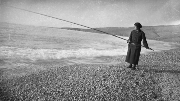 Woman on a beach holding a long pole over the water.