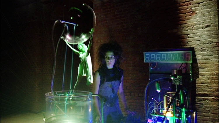 In the foreground, a hologram of a woman holding a transluscent bubble. In the background, a woman surrounded by cables.