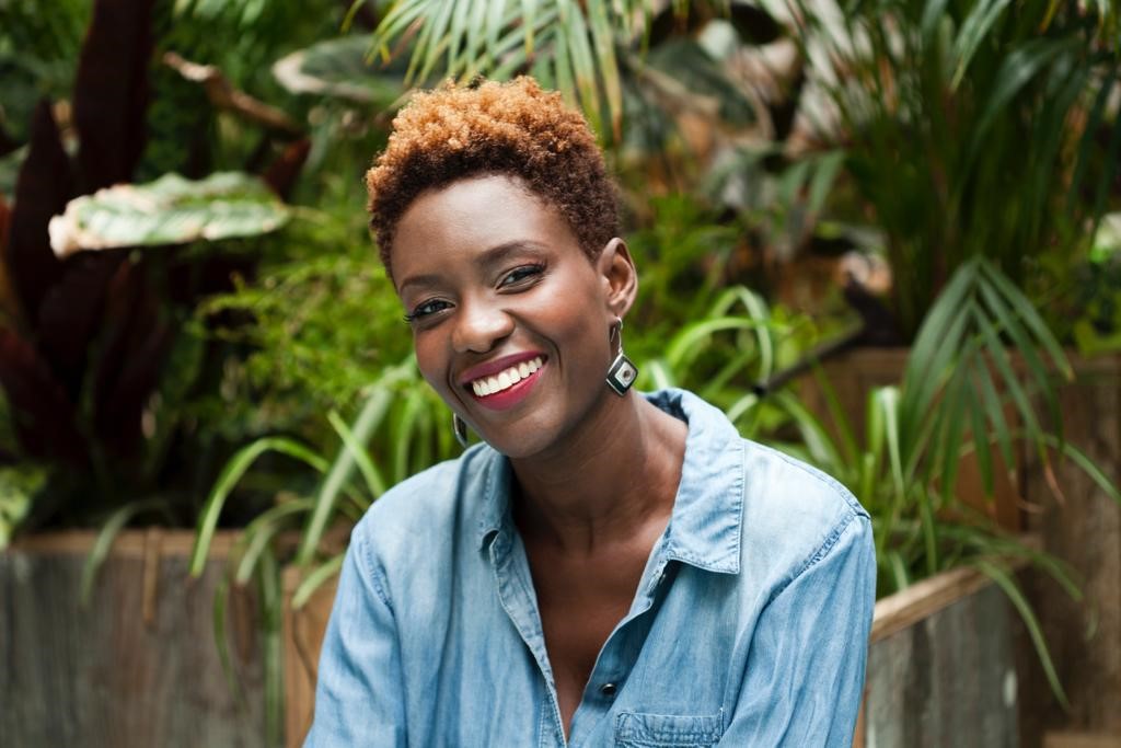 image of Rokhaya Diallo in a blue shirt, behind green foliage. 