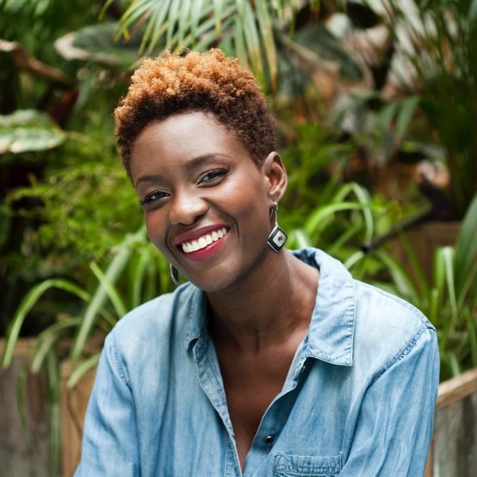portrait photograph of Rokhaya Diallo, in a blue blouse, with with large foliage in the background. 