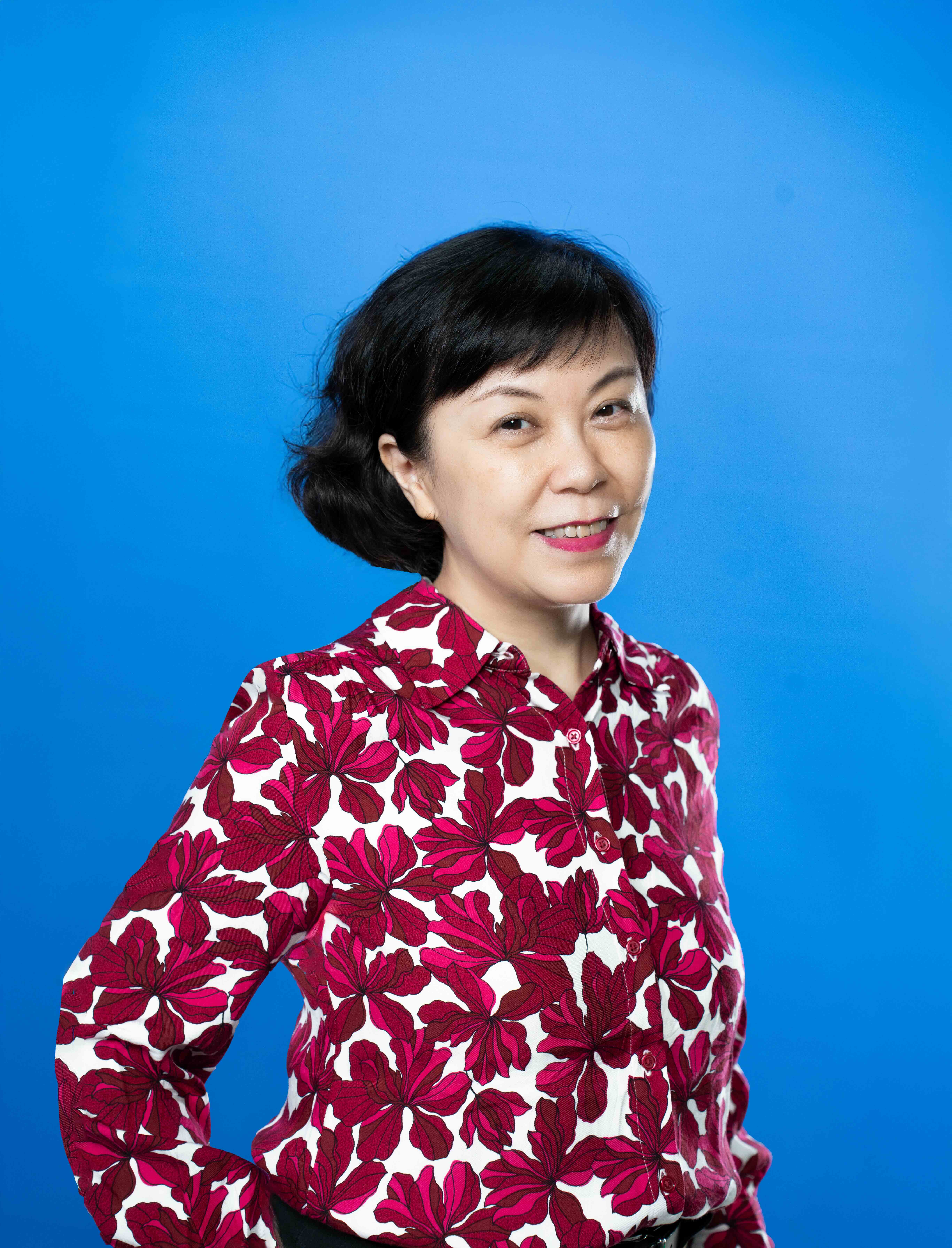 Woman in front of a blue background, wearing a white shirt with red flowers