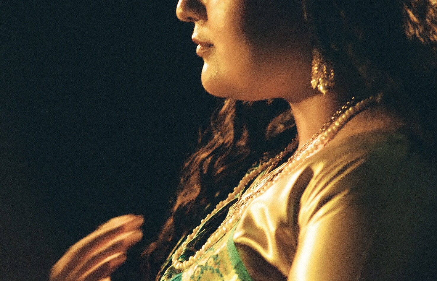 Closeup of the lower half of a woman's face. She is dressed in green and gold. 