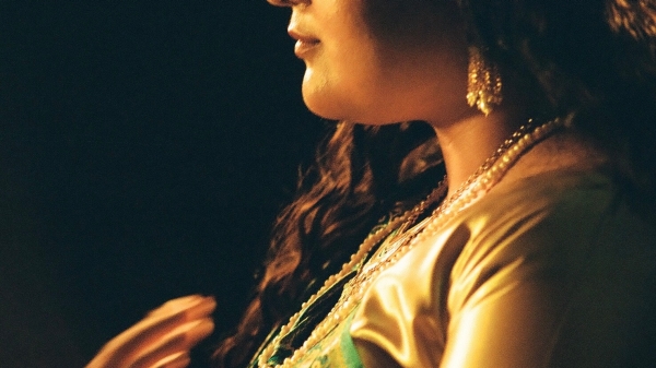 Closeup of the lower half of a woman's face. She is dressed in green and gold. 
