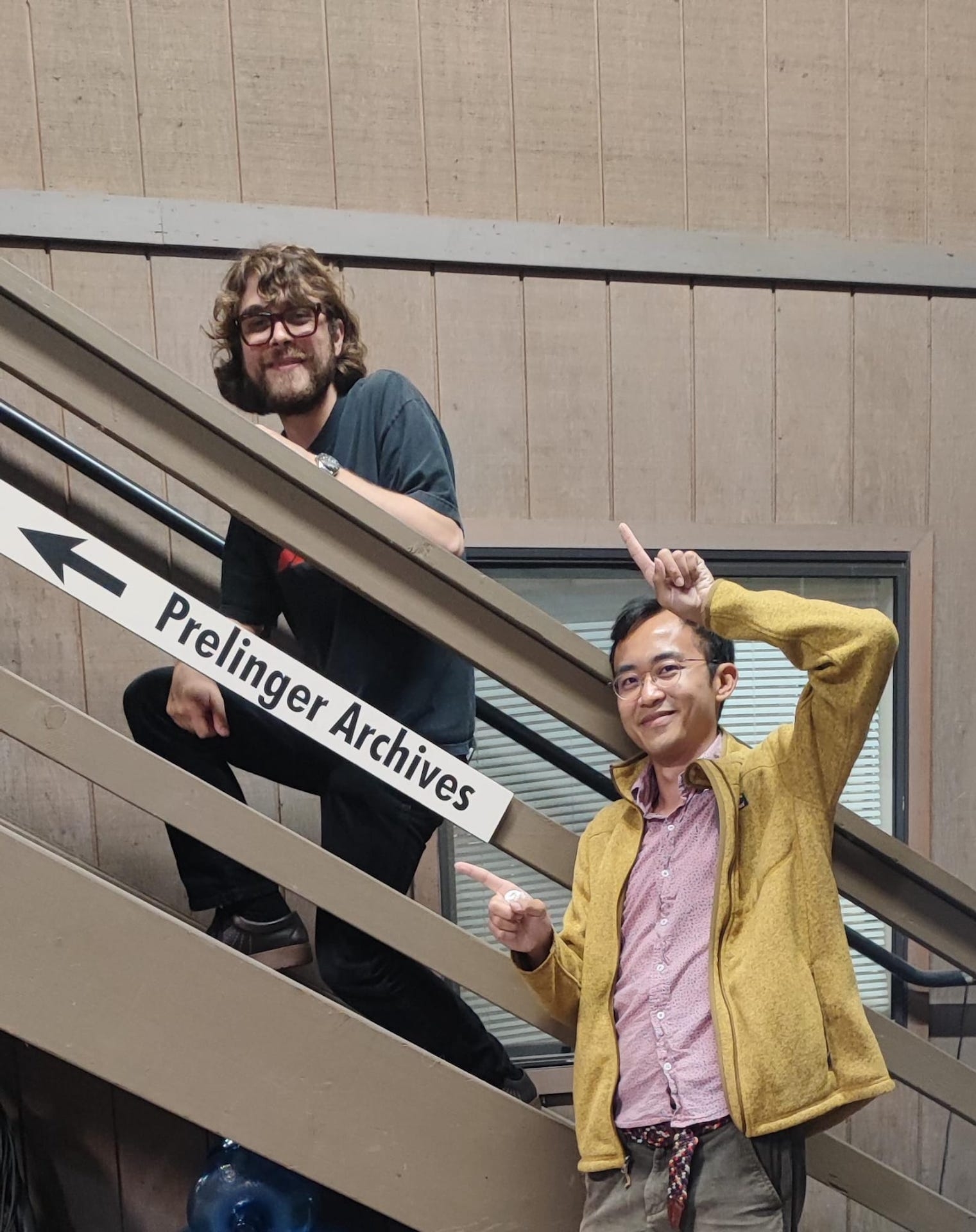 two figures pose for a photo at a staircase