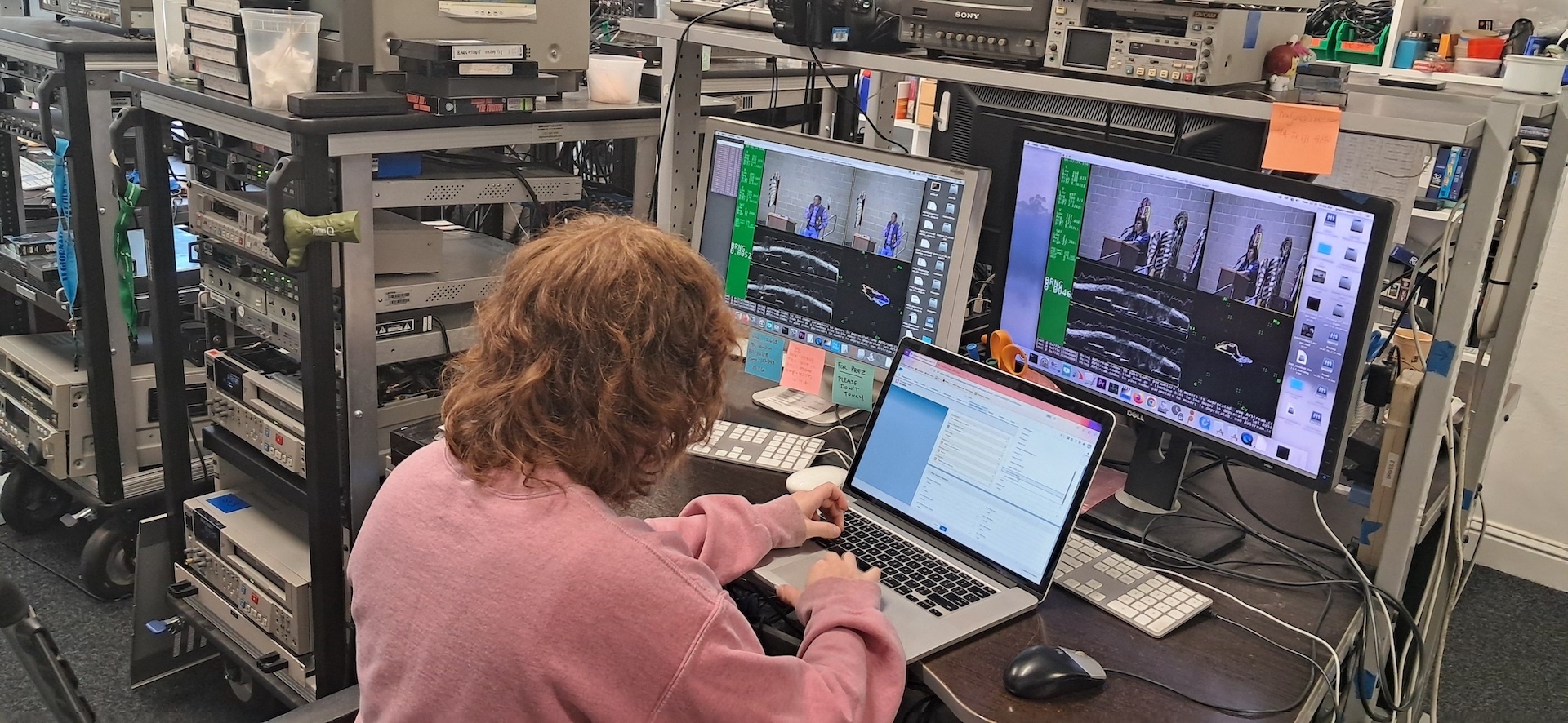 person working at a laptop computer with video rack equipment behind