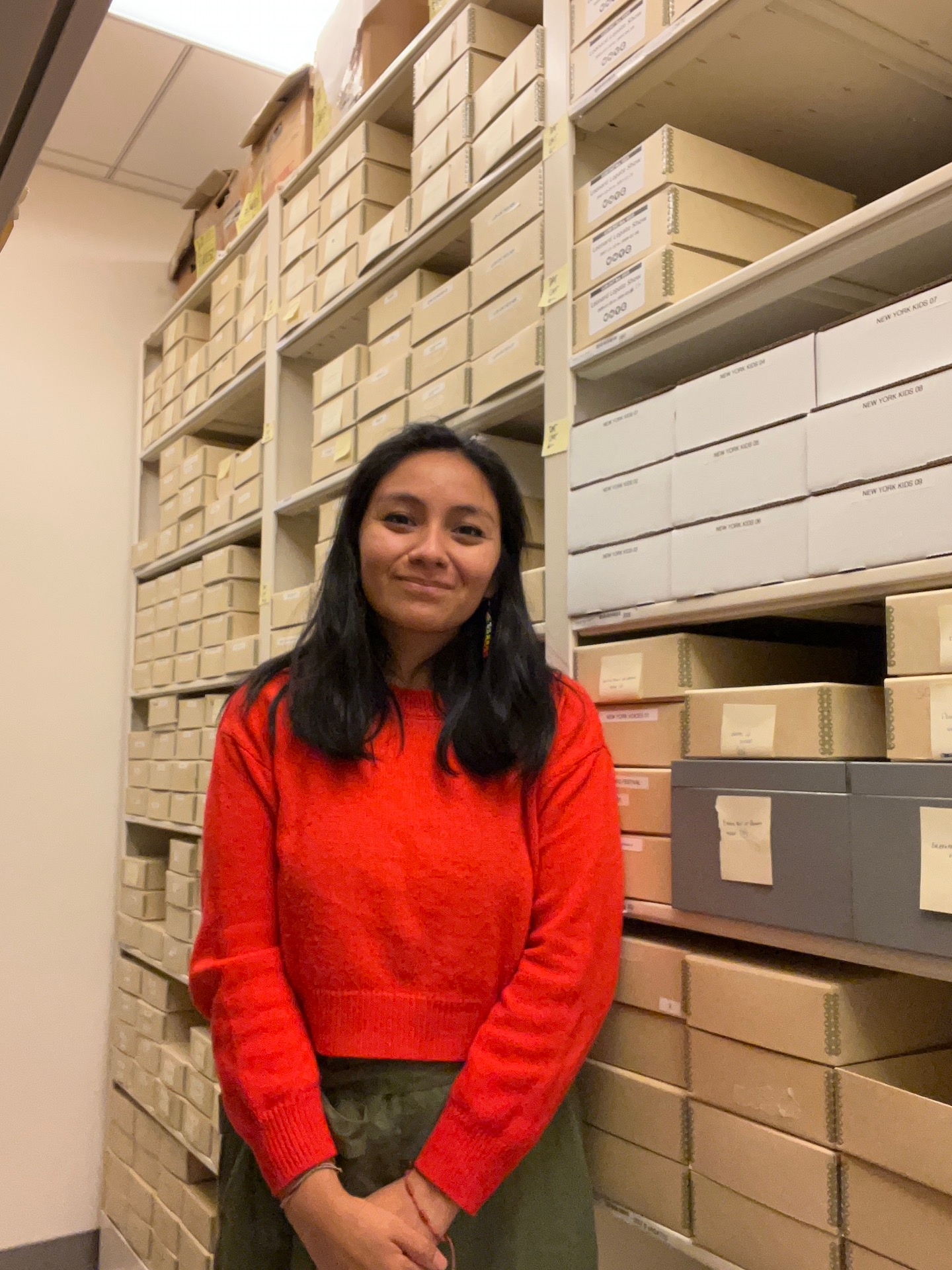 bust-level photo portrait of a woman in a red shirt standing in front of a shelf