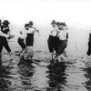Black and white image of men in hats dancing together in shallow water