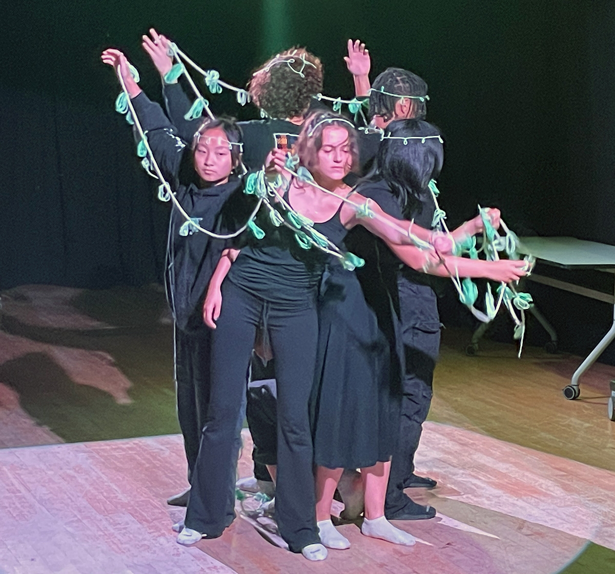 Students dressed in black perform with a green vine wrapped around them
