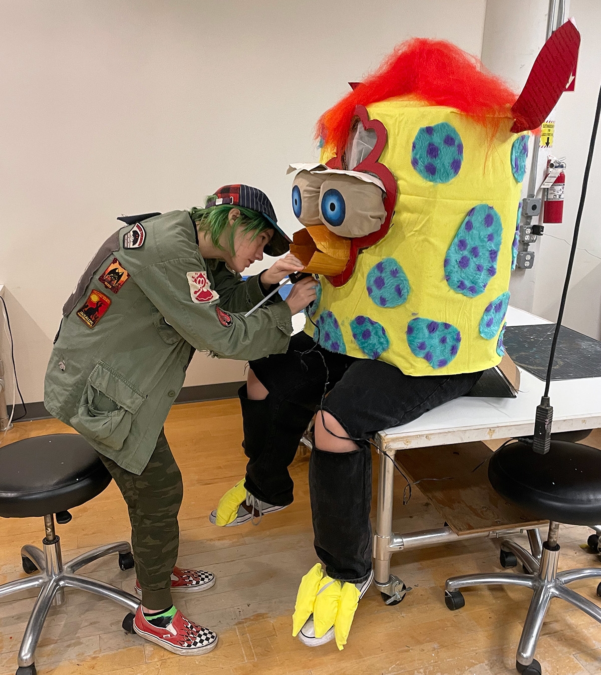 One student helps another put on furby-esque puppet costume