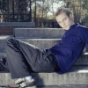 Cadel Martel sits on concrete steps in a park, one leg bent and the other stretched out on the step. He gazes off screen