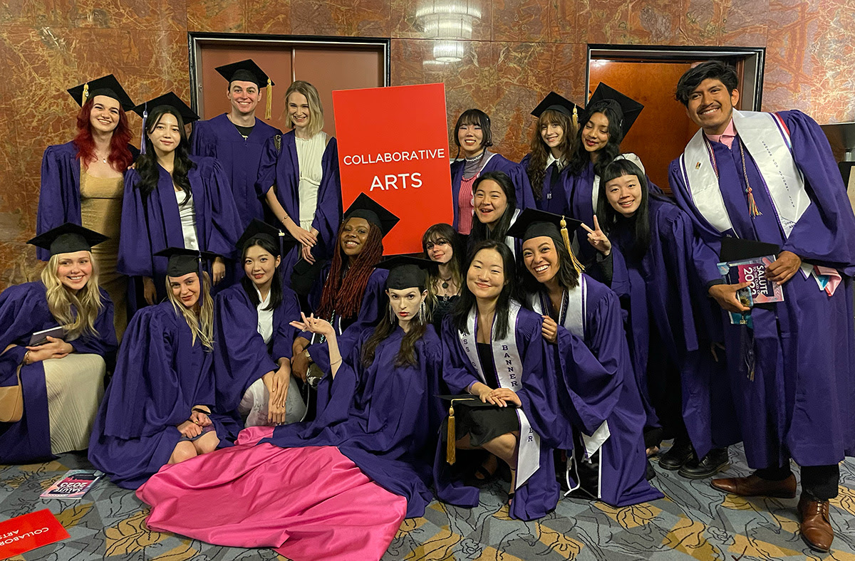 the class of 2023 are gathered around a red Collaborative Arts sign, wearing purple gowns graduation caps
