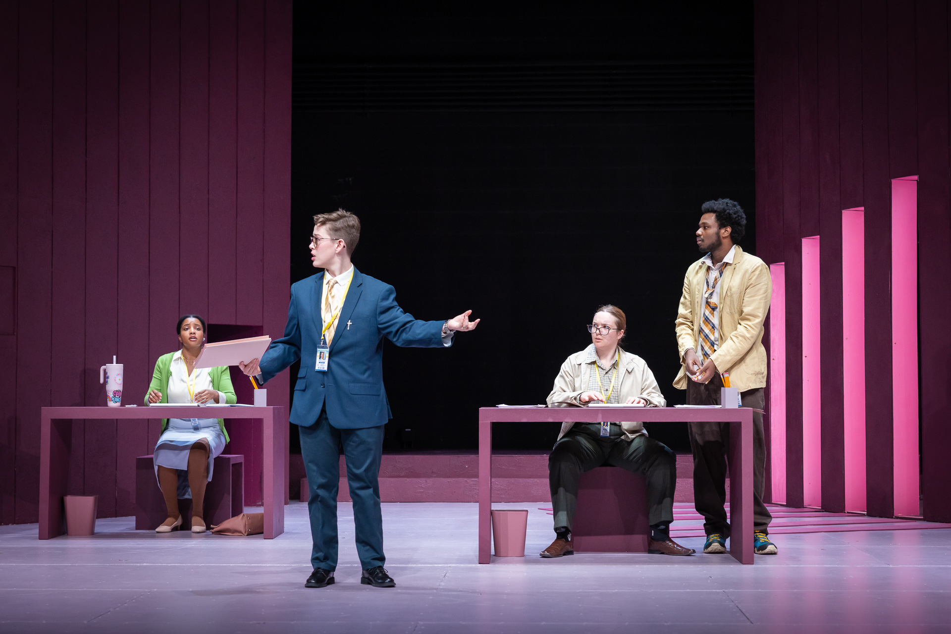 a person in a suit speaking on a stage as others watch