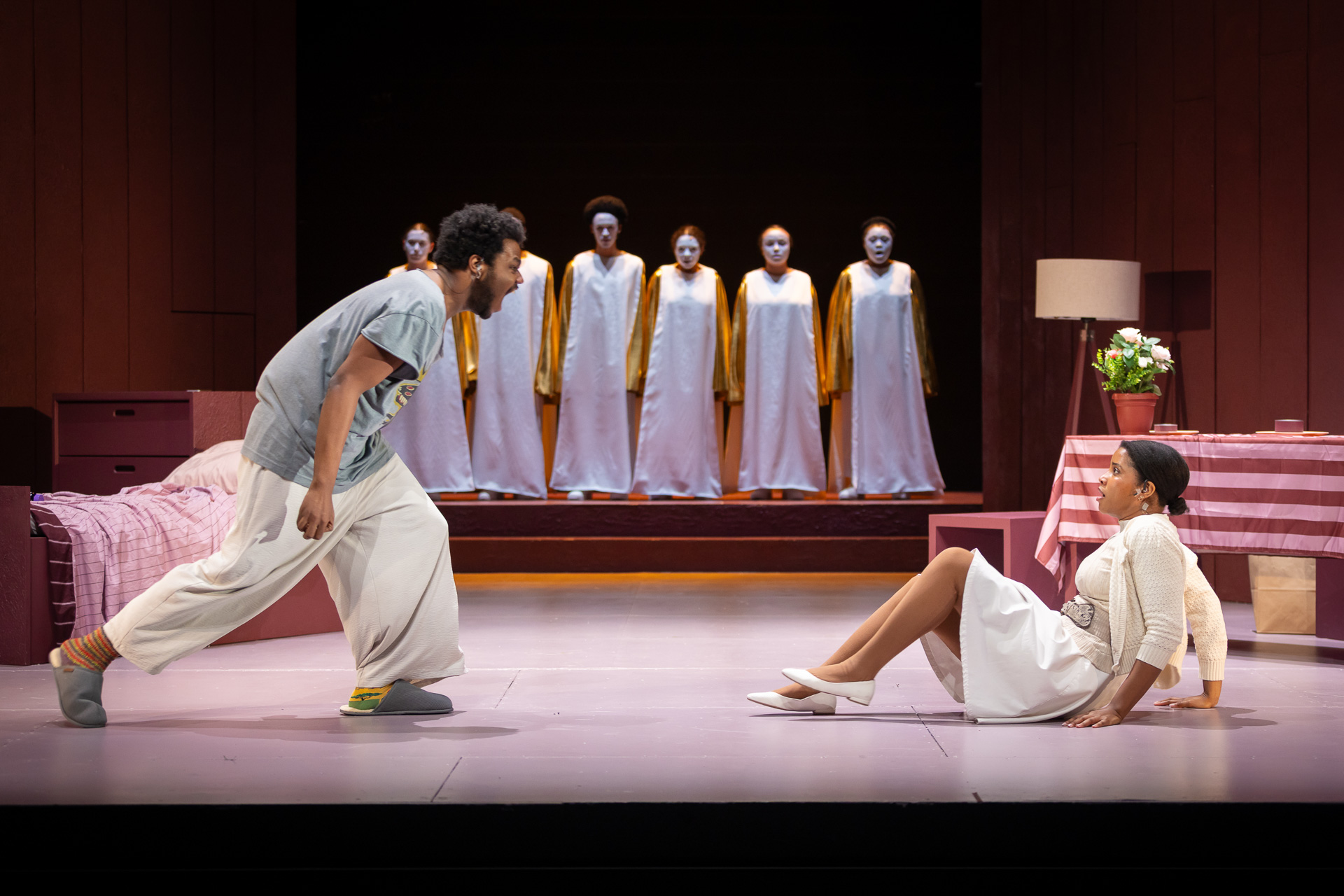 a man yelling at a woman who is on the floor, with people in robes lined up facing the camera