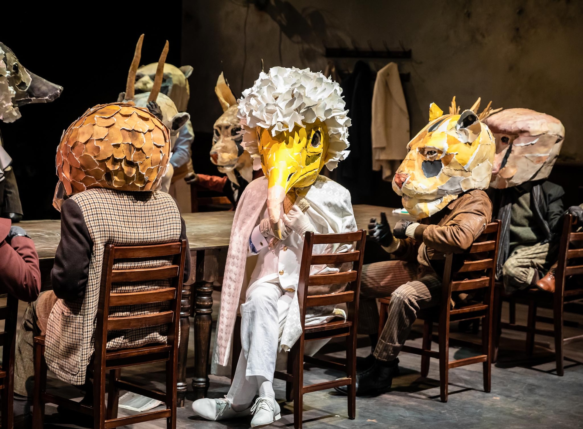 Actors wearing animal masks sitting around a table