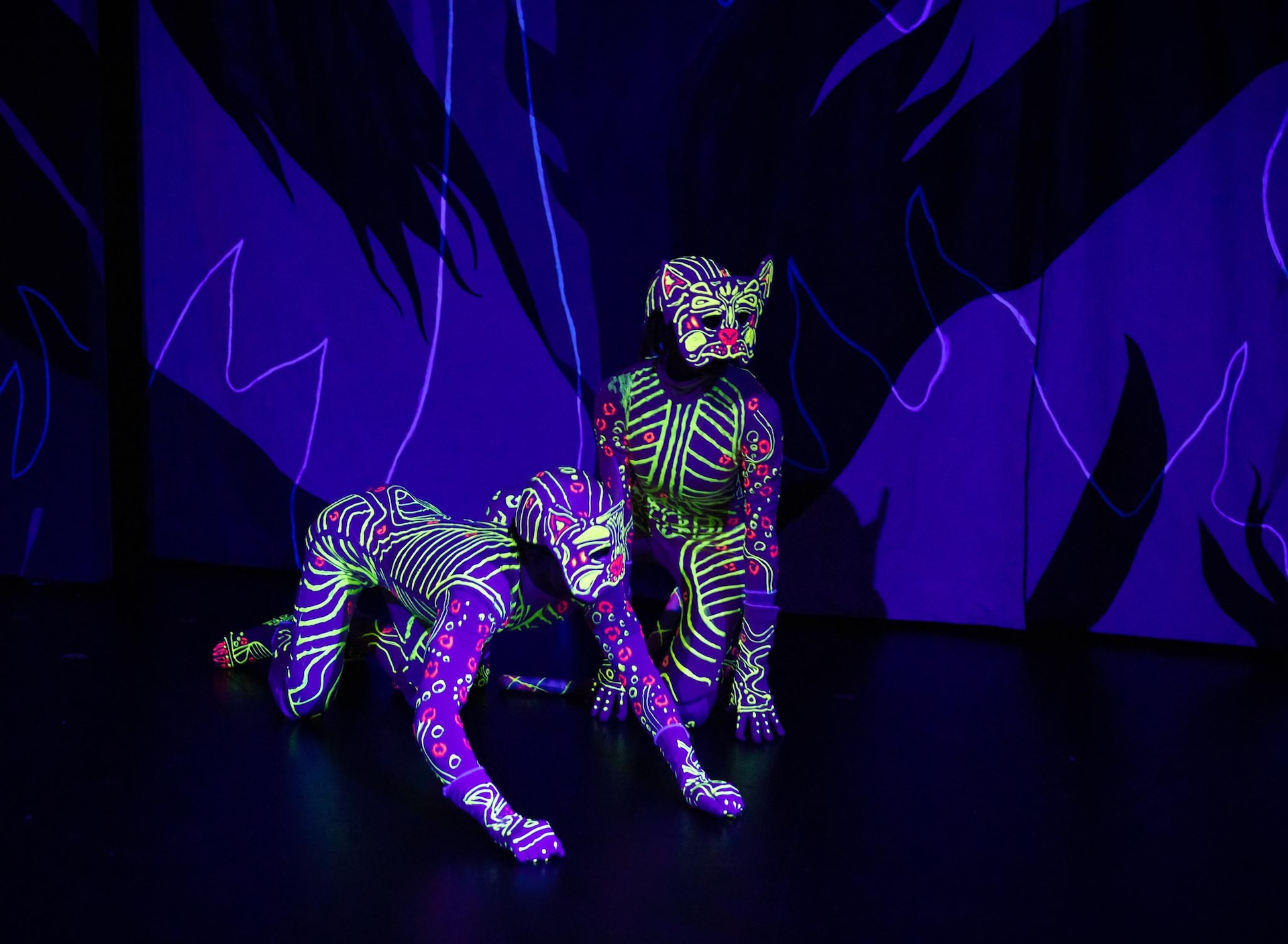 Two actors in neon cat suits onstage