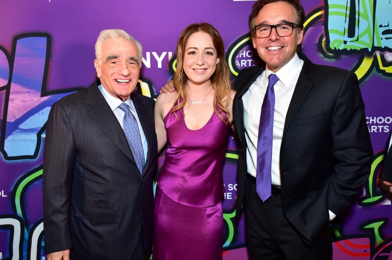 Martin Scorsese in a suit, Eleanor Columbus in a magenta dress, and Chris Columbus in a suit in front of a bright purple step and repeat at the 2018 Tisch Gala