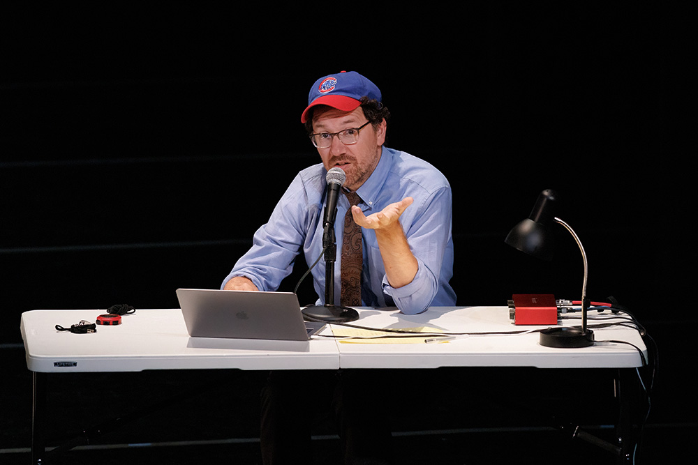 Robbie at desk in front of computer wearing blue and red baseball cap