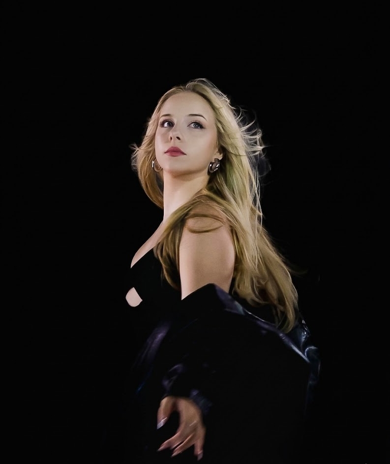 Student with long blonde hair in black dress with black background