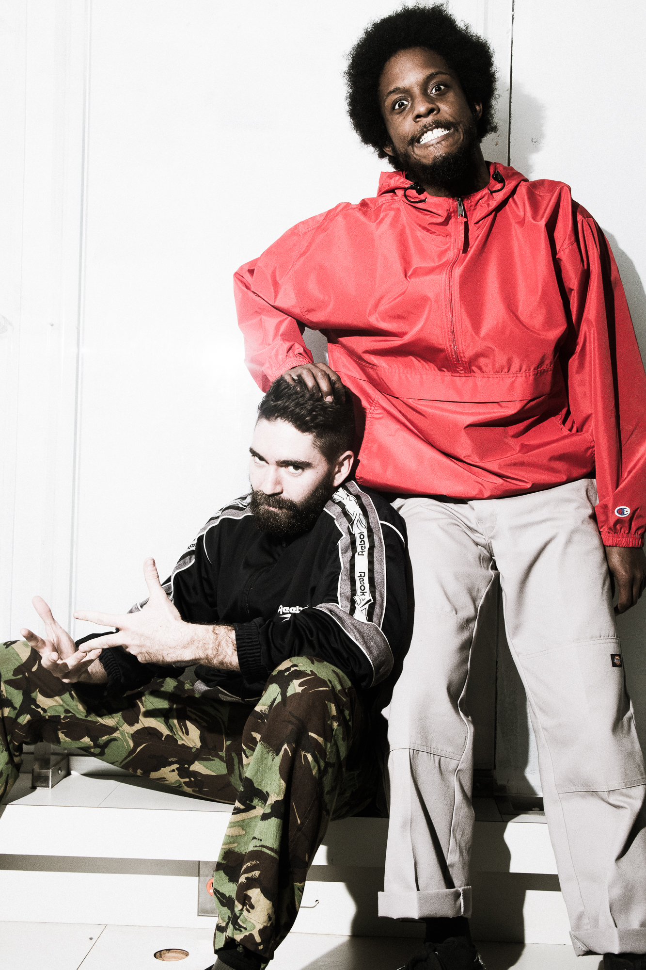 photo of choreographers baye and asa with one individual standing in a red shirt with his hand on the head of his seated partner. 
