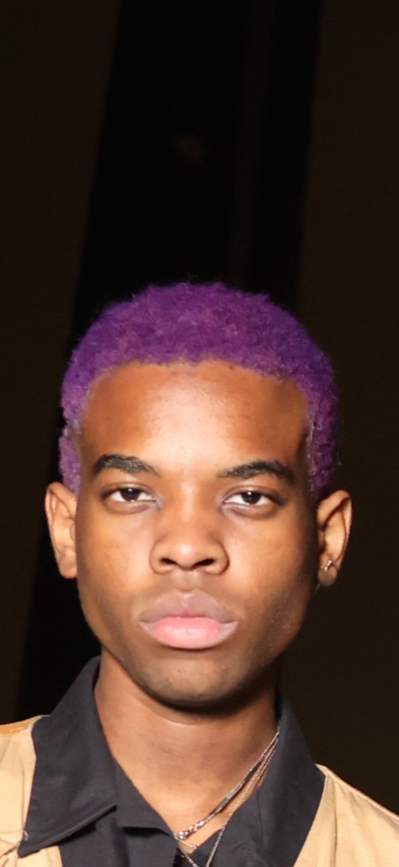 student with short purple hair and dark brown eyes stares directly into the camera