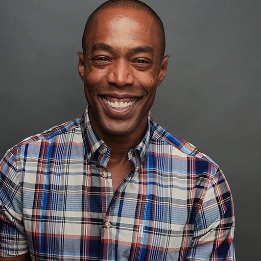 photo of staff member Michael McElroy smiling in a plaid shirt against a gray background