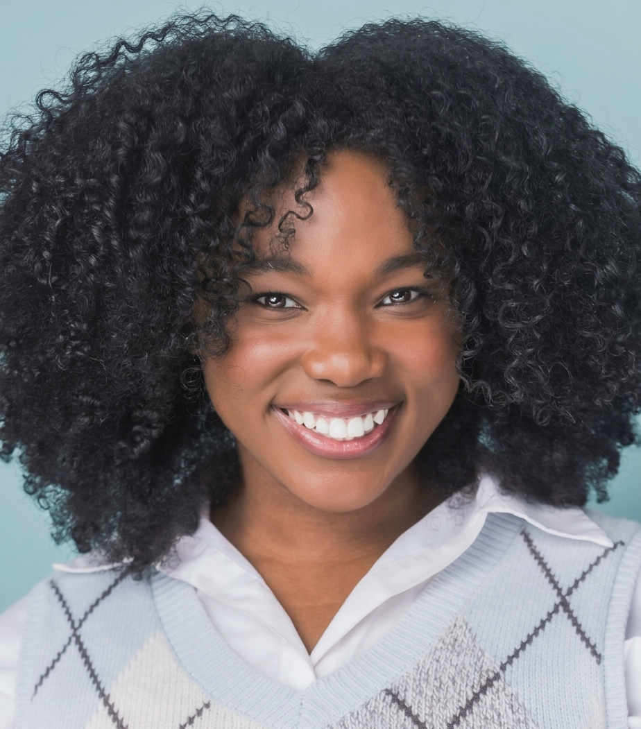 smiling student with curly hair in a sweater with white collared shirt under it. 