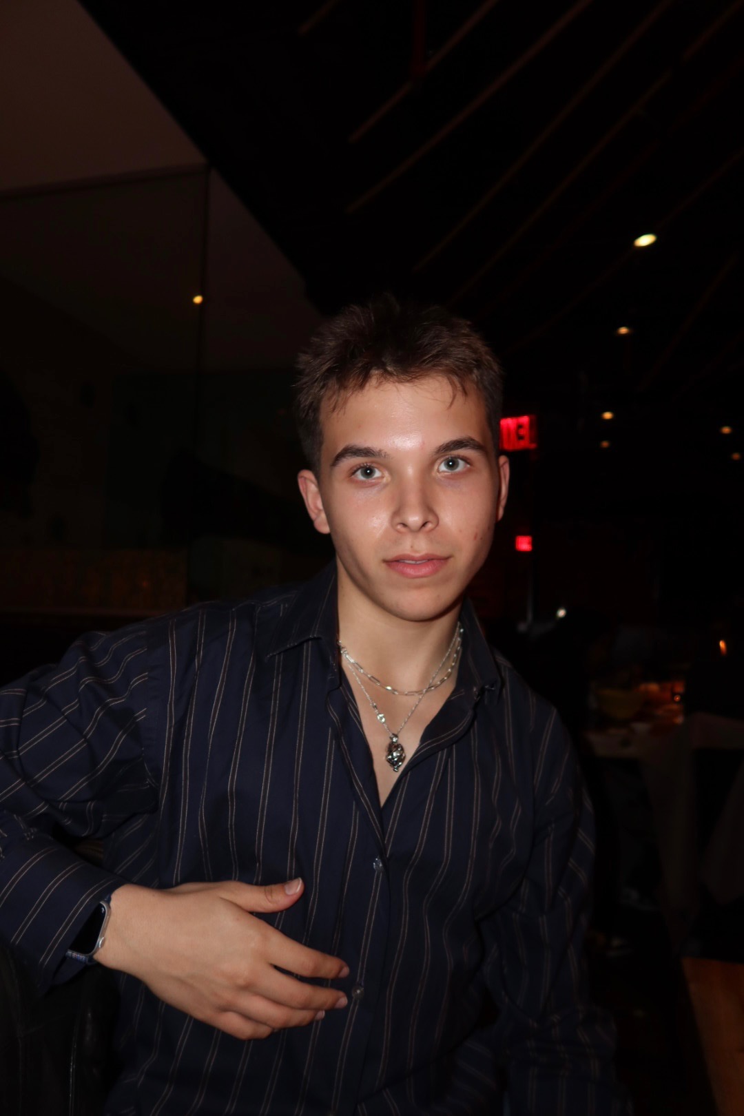 Student with short brown hair in dark button down against a dark background