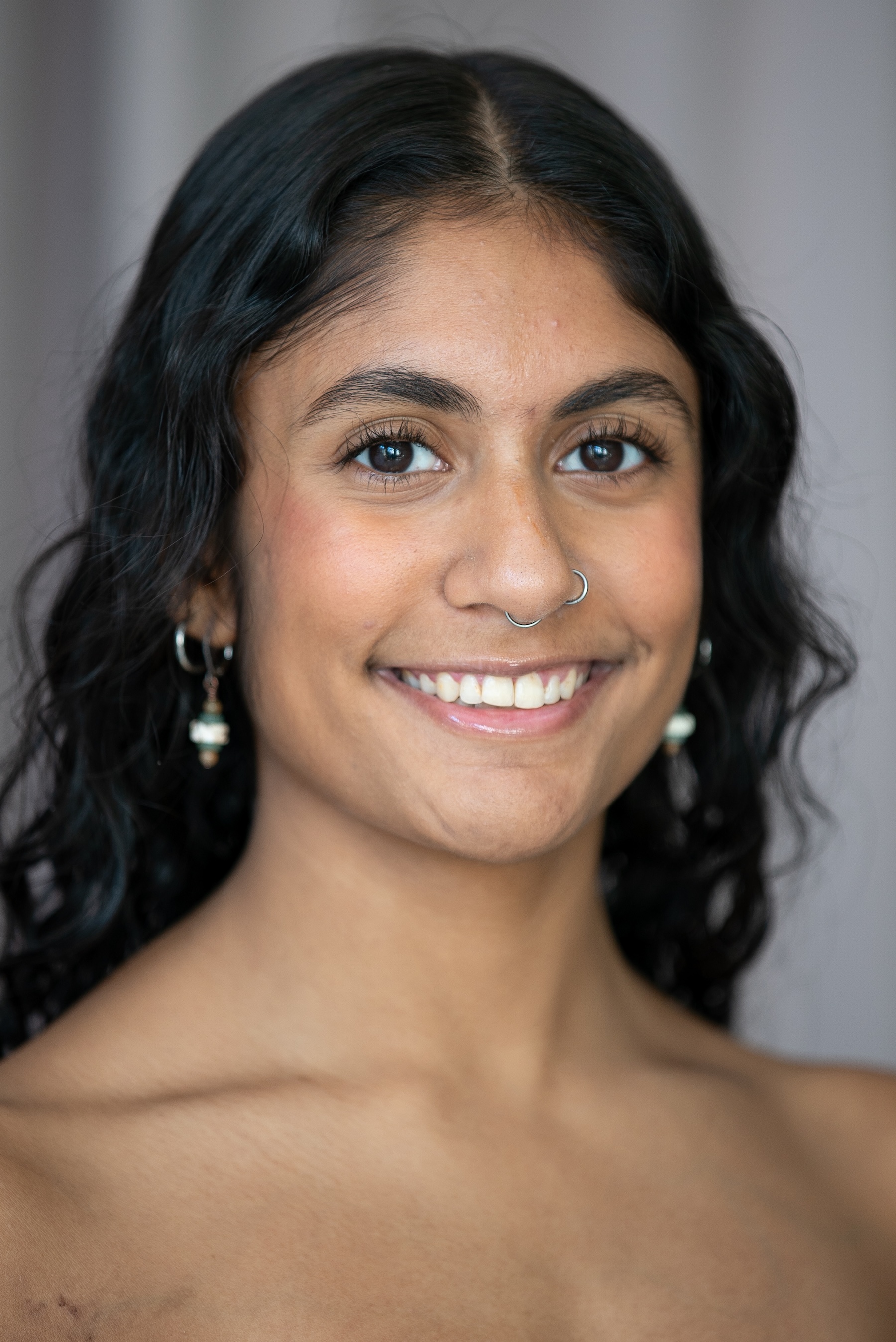 smiling student with white beaded earrings and dark curly hair pushed back on her shoulders. 