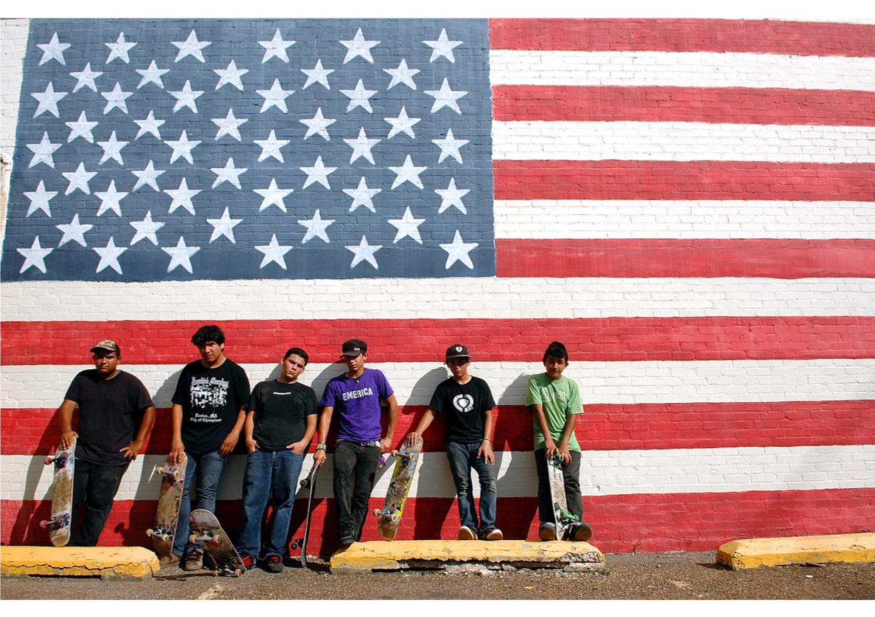 Latino men stand in front of a mural of the American flag