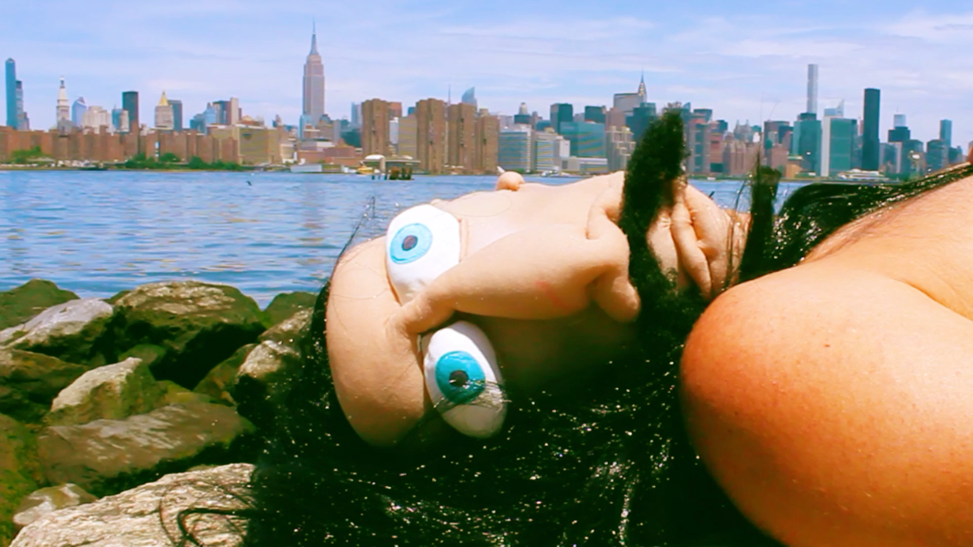 Person with a face mask with a mustache laying next to the east river in NYC.