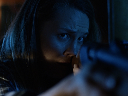 Film Still from Porcupine. Image of close up of woman who is holding up a rifle.