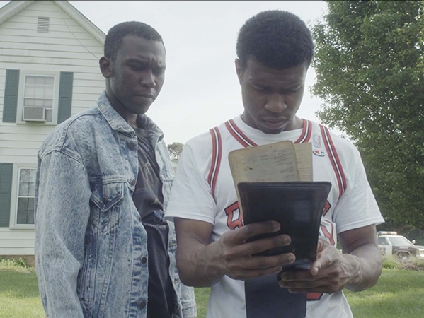 Film Still from Beyond All. Image of two men looking at a ticket book.