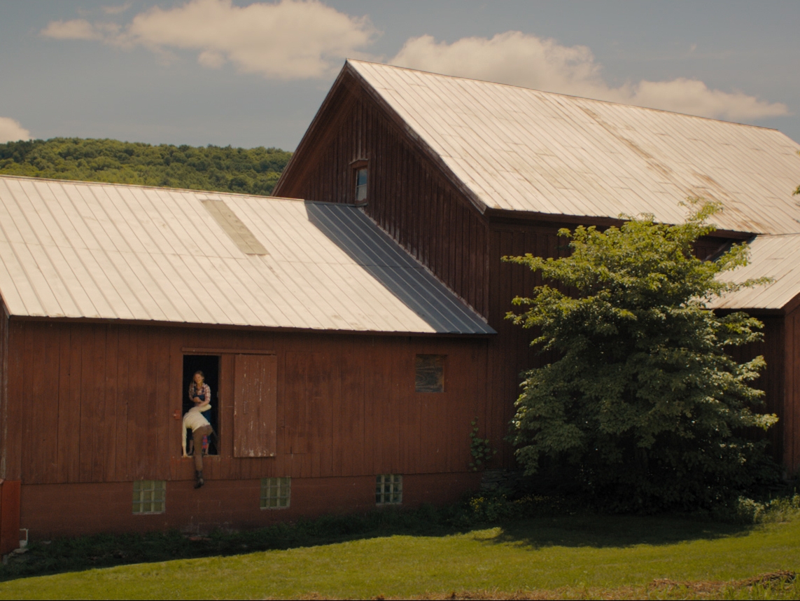 Film Still from Bunny. Image of a red barn with a woman helping a man into it. 