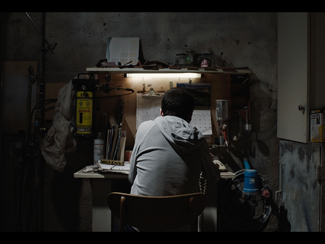 Film Still from The Carpenters. Image of man sitting at a desk from behind. 