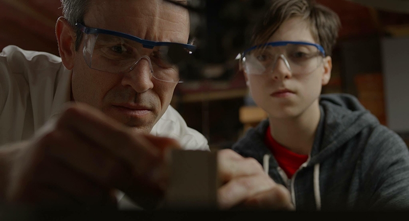 An older man and young boy with work glasses on, working on a project.