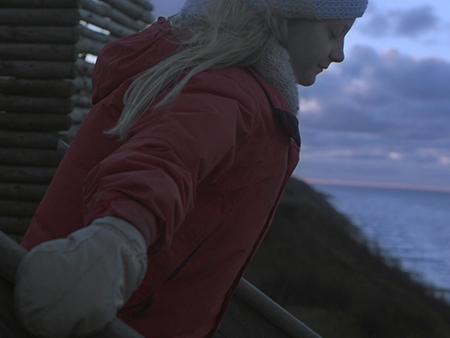 Film Still from Distance. Image of girl walking down steps in winter coat, hat and mittens.