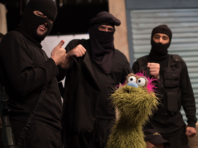 Film Still from Jihadi Street. Image of men dressed in black with masks surrounding a green puppet.