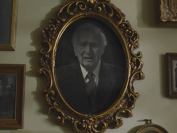 Film still from Killing the Fiddler. Image of framed photo of an old man. 