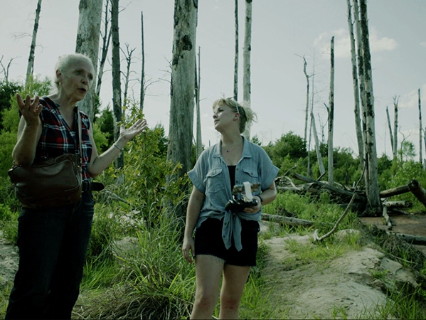 Film Still from perennials. Image of older and younger women in a sparse wooded area. 