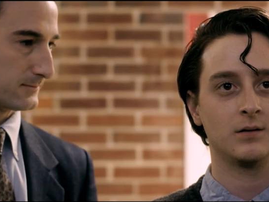 Film Still from Richard. Image of close up of two men's faces dress in suits.