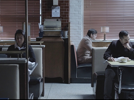 Film still from The Spotter. Image of inside of a diner with 3 people sitting at individual tables alone.. 