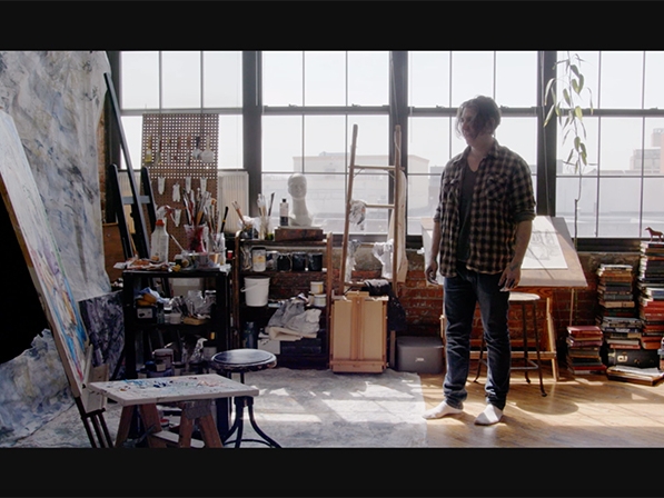 Film still from Vivid. Image of man in painting studio staring at a large canvas.