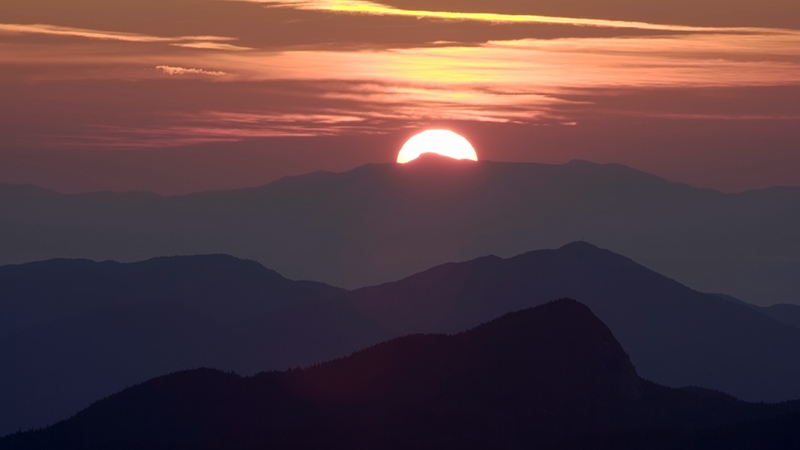 An image of the sun setting behind a mountain landscape.