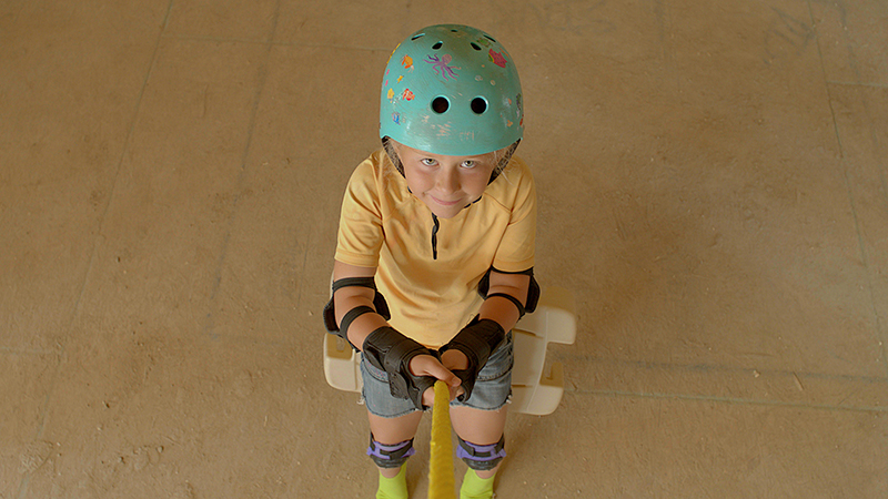 An image of a little girl in a bike helmet and knee pads, looking upwards.