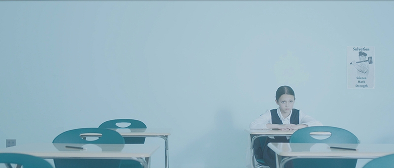 A lone girl, sitting at a desk in a classroom.